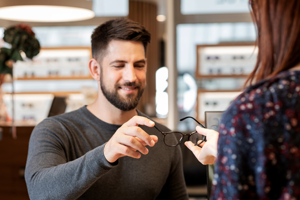 Man in an eyewear store hands a pair of glasses to a customer.